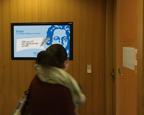 ein digitaler Bildschirm in einer Bibliothek mit Menschen in der Nähe